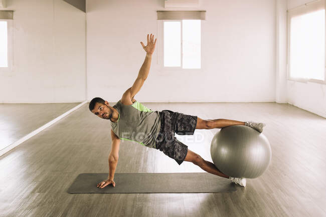 Longitud completa de un fuerte deportista muscular haciendo Side Star Plank en la pelota en forma durante el entrenamiento en el estudio - foto de stock
