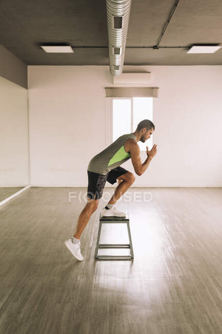 Вид сбоку серьезного молодого спортивного мужчины в спортивной одежде, выполняющего упражнение One Leg Squat на ступеньке во время тренировки в студии — стоковое фото