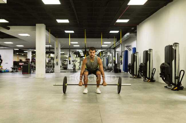 Полное тело сильного молодого мускулистого спортсмена в спортивной форме, поднимающего штангу во время интенсивной тренировки в современном тренажерном зале — стоковое фото