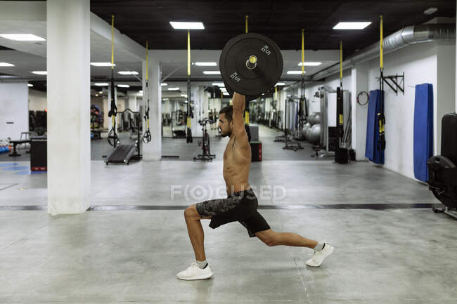 Side view of full body of strong young muscular male athlete in activewear lifting barbells during intense workout in modern gym — Stock Photo