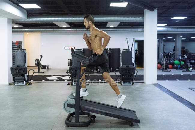 Visão lateral corpo inteiro de homem forte e duradouro treinamento em equipamentos esportivos em ginásio espaçoso — Fotografia de Stock