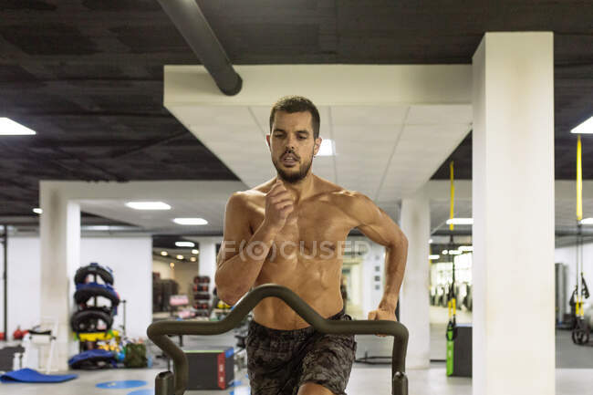 Vista frontal de un fuerte entrenamiento de hombre duradero en equipos deportivos en un amplio gimnasio - foto de stock