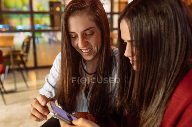 Jovem alegre casal lésbico sentado à mesa no café e usando smartphone enquanto passam o fim de semana juntos — Fotografia de Stock