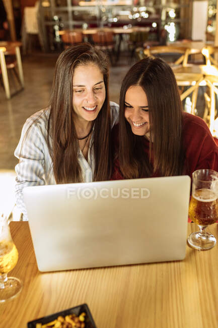 Angle élevé de couple de lesbiennes enchanté assis à table dans un café et regardant un film drôle sur un ordinateur portable tout en profitant du week-end ensemble — Photo de stock