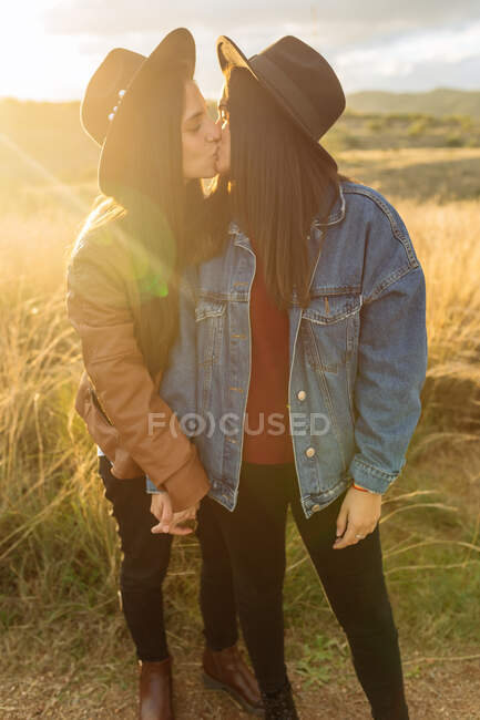 Vista lateral de joven pareja lesbiana de pie en el campo y besándose tiernamente con los ojos cerrados - foto de stock