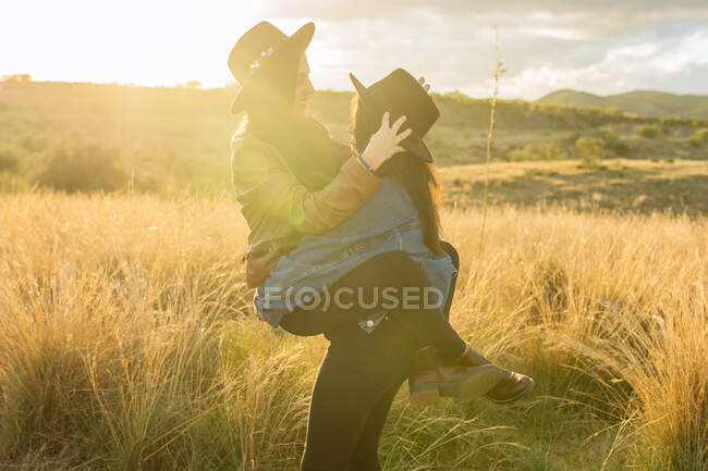 Seitenansicht eines fröhlichen lesbischen Paares, das Spaß auf dem Feld hat, während es sich umarmt und das Wochenende zusammen verbringt — Stockfoto