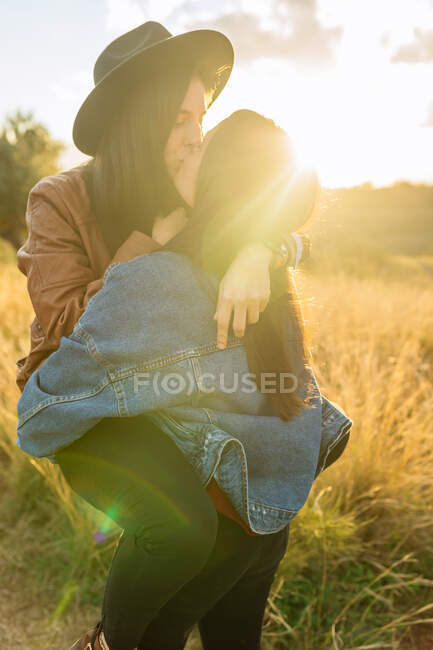 Side view of cheerful lesbian couple having fun in field while embracing and spending weekend together — Stock Photo