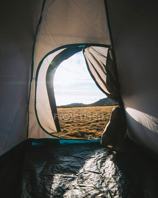Tenda de acampamento com porta aberta colocada no prado gramado perto de colinas contra o céu azul nublado na manhã ensolarada — Fotografia de Stock