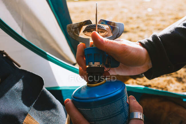 Side view of anonymous calm young male camper in casual clothes preparing the stove for hot drink while resting in tent after hiking in mountains on sunny day — Stock Photo