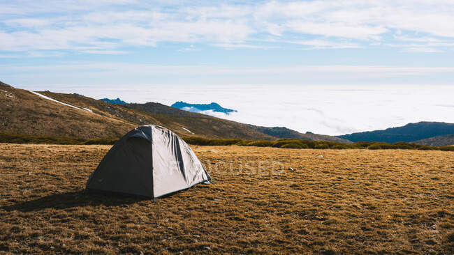 Paysage pittoresque de tente de camping placée sur une pente herbeuse dans une vallée montagneuse enneigée contre un ciel nuageux au soleil — Photo de stock