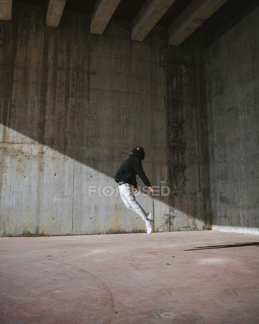 Side view of unrecognizable guy in stylish casual outfit and face mask performing dance movement in shabby abandoned building in sunlight — Stock Photo
