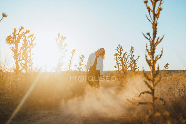 Боковой вид активной юной леди в модном наряде танцующей в сухих извергах против безоблачного голубого неба в сельской местности — стоковое фото