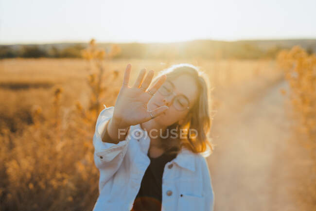 Front view of active young lady in trendy outfit showing hand in dry fiends against cloudless sky in countryside — Stock Photo
