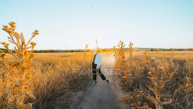 Side view of active young lady in trendy outfit dancing in dry fiends against cloudless blue sky in countryside — Stock Photo