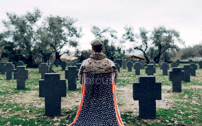 На задньому плані зображено повне тіло солдата в уніформі, який сидить на стільці з американським прапором і оплакує смерть воїнів на кладовищі. — стокове фото