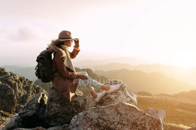 Vista lateral de un excursionista irreconocible sentado en piedra y observando increíbles paisajes del valle de las tierras altas en un día soleado - foto de stock