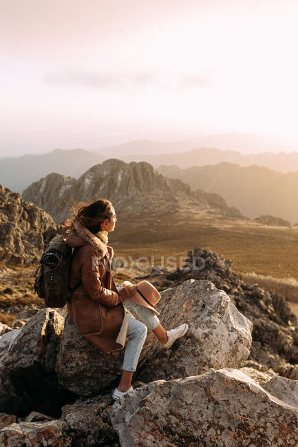 Vista lateral do caminhante irreconhecível sentado em pedra e observando paisagens incríveis do vale das terras altas no dia ensolarado — Fotografia de Stock