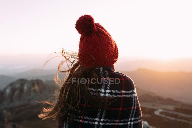 Vista trasera de excursionista irreconocible en manta de pie sobre piedra y observando paisajes increíbles del valle de las tierras altas en un día soleado - foto de stock