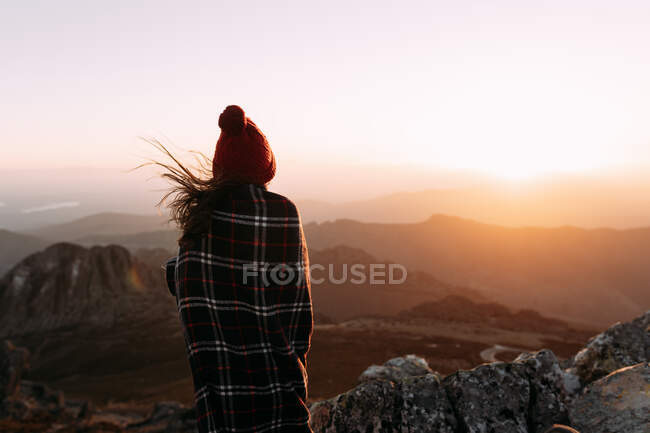 Back view of unrecognizable hiker in blanket standing on stone and observing amazing scenery of highlands valley on sunny day — Stock Photo
