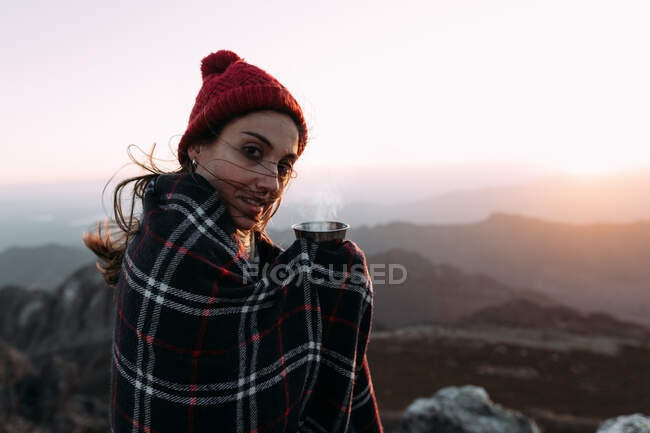 Vista laterale di escursionista in coperta bere caffè caldo e in piedi sulla pietra e osservare paesaggi incredibili della valle degli altopiani nella giornata di sole — Foto stock