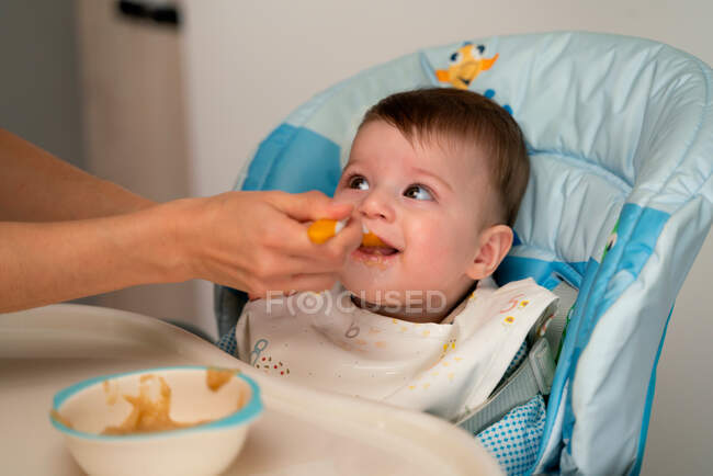 Чарівна щаслива дитина в колясці сидить і годується солодкою дитячою їжею від матері — стокове фото