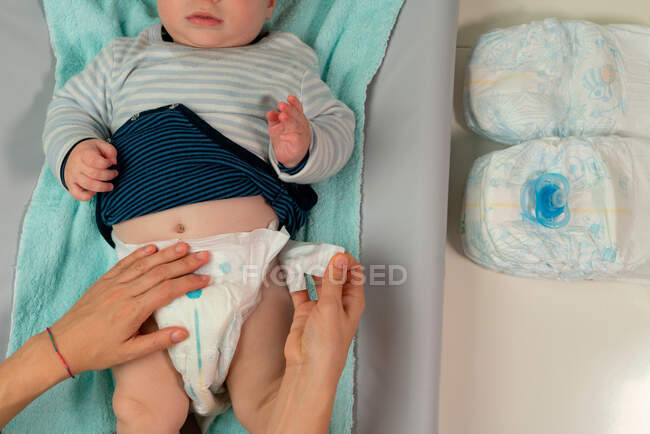 Sorgende Mutter wechselt Windel auf niedlichem Baby, das zu Hause auf Wickeltisch liegt — Stockfoto