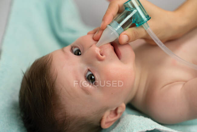 Crop mère attentionnée plaçant la machine d'aspiration dans la narine de bébé adorable pour enlever le mucus — Photo de stock