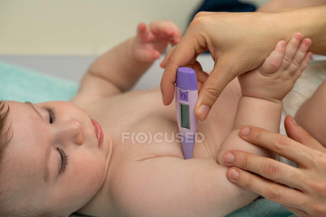Cultivar mãe amorosa medir a temperatura do bebê bonito e colocar o termômetro na axila do bebê com cuidado — Fotografia de Stock