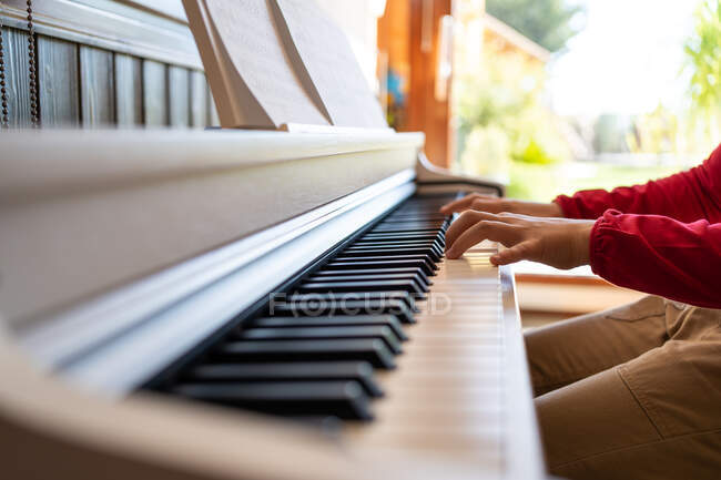 Cropped anonymous child playing piano while reading notes and rehearsing song at home — Stock Photo