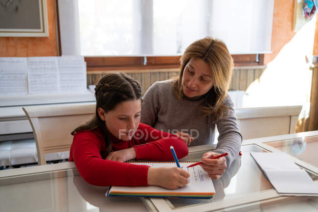 Mutter hilft Tochter bei Hausaufgaben, während sie mit Notizbuch am Tisch sitzt und zu Hause lernt — Stockfoto