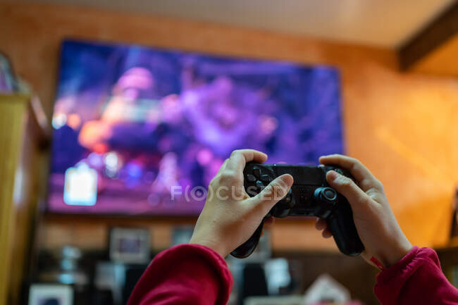 Crop persona anonima con controller giocare ai videogiochi in camera con grande schermo TV, mentre intrattenere nel fine settimana a casa — Foto stock