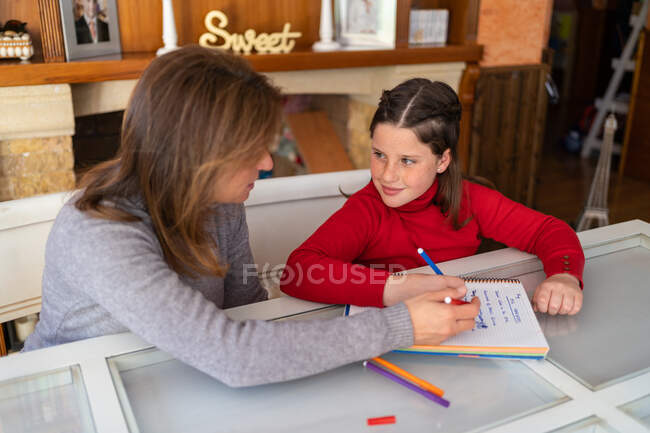 Angle élevé de la mère aider sa fille à faire ses devoirs tout en étant assis à table avec un cahier et en étudiant à la maison — Photo de stock