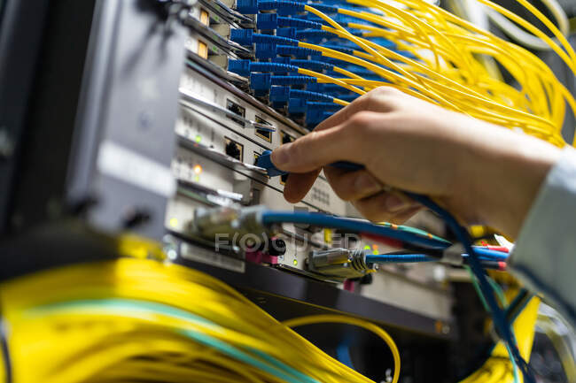 De baixo da colheita homem anônimo colocando cabo eletrônico no sistema de dados na sala de comunicações — Fotografia de Stock