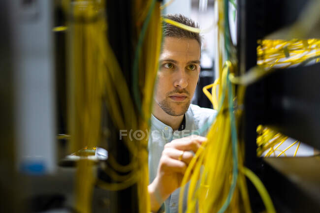 Концентровані фахівці чоловічої статі, що працюють з дротами на сервері, керуючи мережею в центрі обробки даних — стокове фото