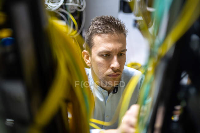 Concentrated male specialists working with wires in server while managing network in data center — Stock Photo