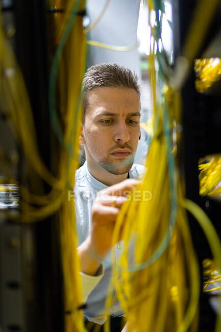 Концентровані фахівці чоловічої статі, що працюють з дротами на сервері, керуючи мережею в центрі обробки даних — стокове фото