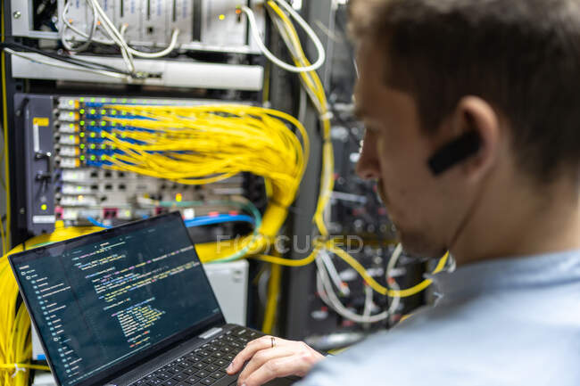 Задний вид сеялки мужчина помощник прокладки кабеля в роутер при использовании ноутбука для проверки сетевой системы — стоковое фото