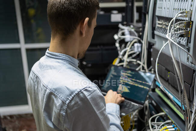 Задний вид сеялки мужчина помощник прокладки кабеля в роутер при использовании ноутбука для проверки сетевой системы — стоковое фото