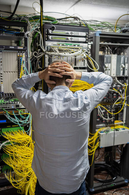 Rückansicht eines nicht wiederzuerkennenden männlichen Technikers, der nach dem Kopf greift, während er Probleme im Rechenzentrum mit Serverschränken hat — Stockfoto