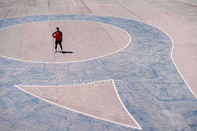 De cima de jogador de basquete descansando com bola na quadra de concreto durante as habilidades de treinamento em dia ensolarado — Fotografia de Stock