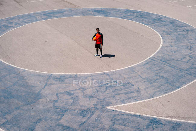 D'en haut du joueur de basket-ball se reposant avec la balle sur le terrain en béton pendant les compétences d'entraînement dans la journée ensoleillée — Photo de stock