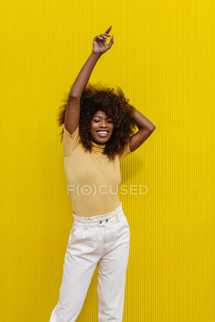 Porträt einer schwarzgelockten Frau mit erhobenen Armen vor gelbem Hintergrund — Stockfoto