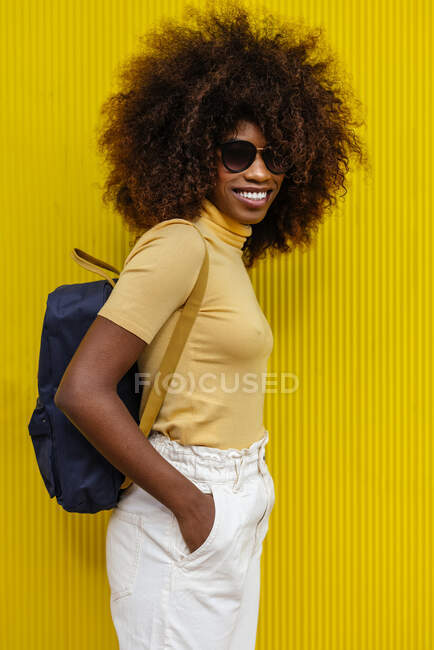 Retrato de una mujer negra de pelo rizado mirando a la cámara delante de un fondo amarillo - foto de stock
