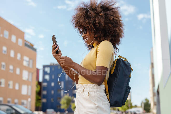 Чорна жінка з афро волоссям слухає музику на мобільному телефоні з рюкзаком на спині — стокове фото
