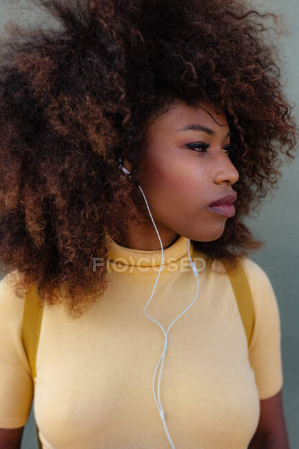 Mujer negra con pelo afro escuchando música con una mochila en la espalda - foto de stock