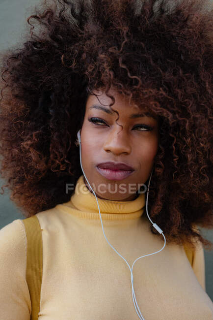 Mujer negra con pelo afro escuchando música con una mochila en la espalda - foto de stock