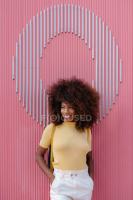 Черная женщина с афроволосами, позирующая перед розовой стеной, смотрит в сторону — стоковое фото