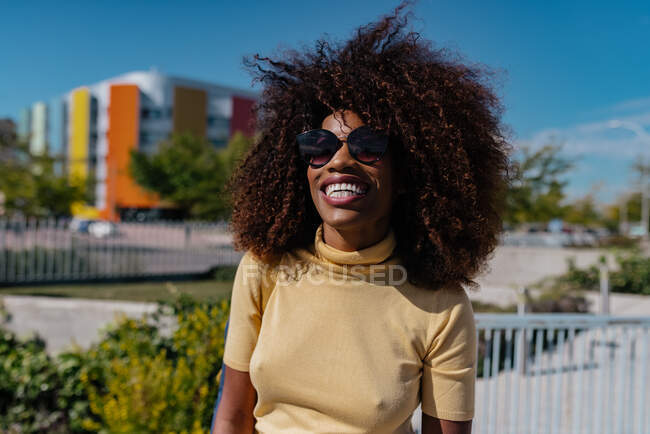 Mujer negra con el pelo rizado caminando por la calle y riendo felizmente - foto de stock