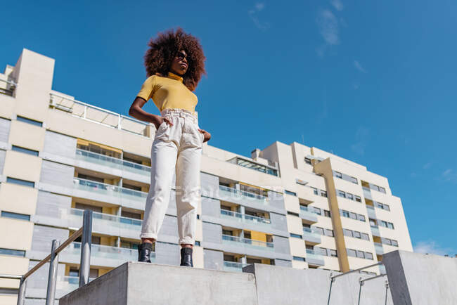 Black woman with curly hair standing on a wall in the street and laughing happily — Photo de stock