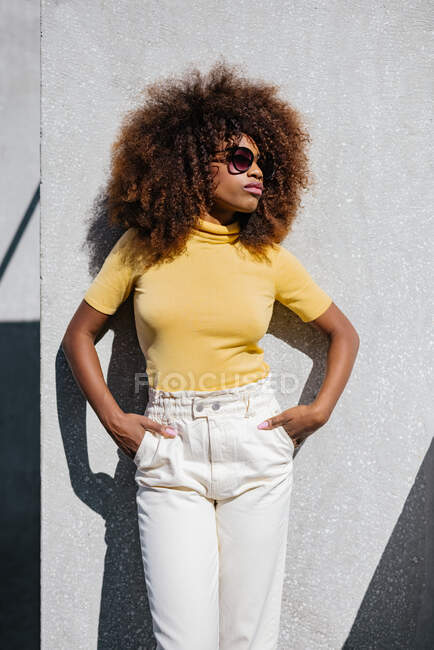 Donna nera con capelli afro posa davanti a un muro grigio guardando altrove — Foto stock